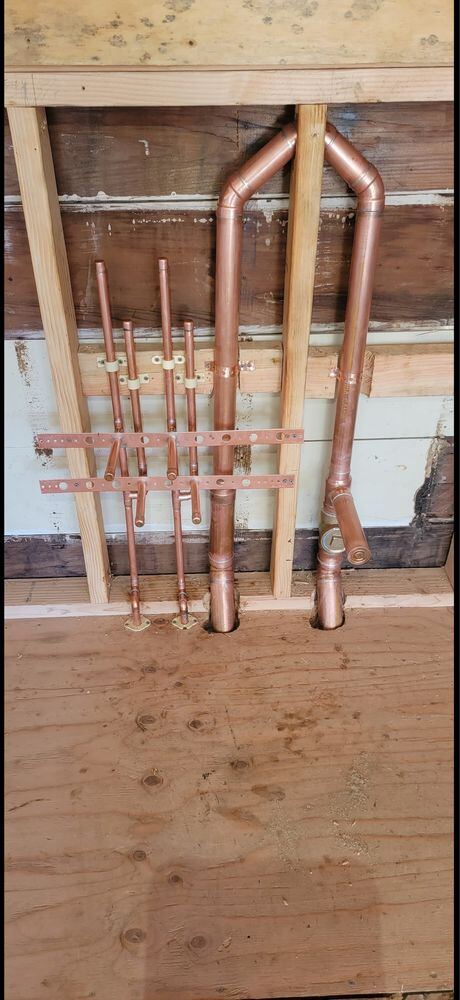New copper repipe manifold with shutoff valves installed in a residential wall before drywall