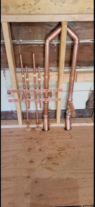 New copper repipe manifold with shutoff valves installed in a residential wall before drywall